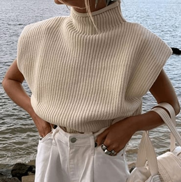 Model at the beach, wearing the Apricot Luckinbaby Casual Women’s Knit Sweater Vest with white pants and a white bag