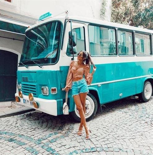 Influencer Eylem Abaci leaning against a vintage green bus and wearing cutoff shorts and a wrap top