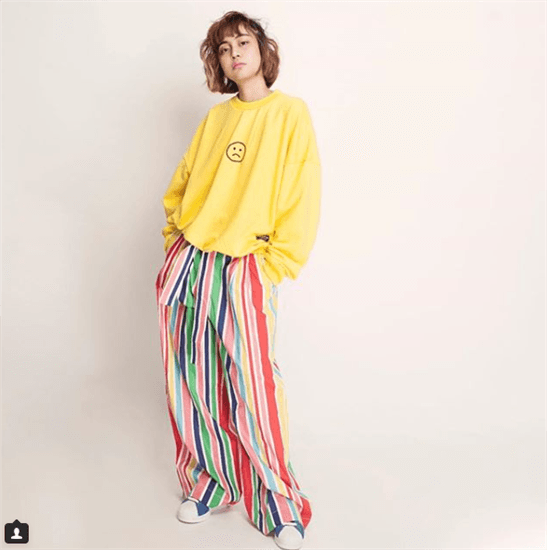 Influencer Evita Nuh wearing striped baggy pants and yellow sweatshirt with frowny face