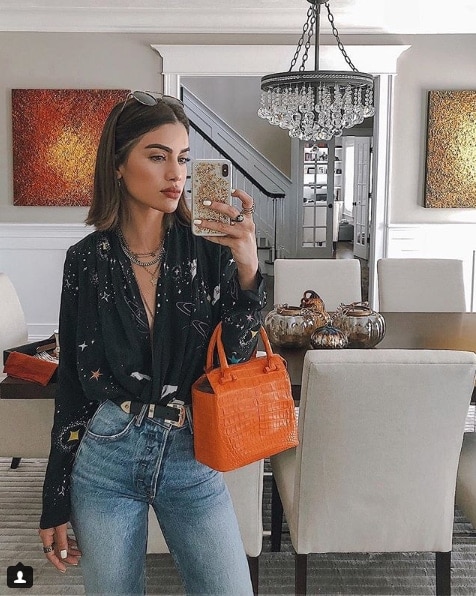 Influencer Camila Coelho taking mirror selfie in home holding orange crocodile print bag 
