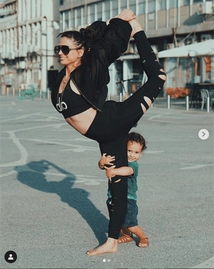 Israeli yoga instructor and influencer Talia Sutra holding a yoga pose with son, Akiva, hugging her leg