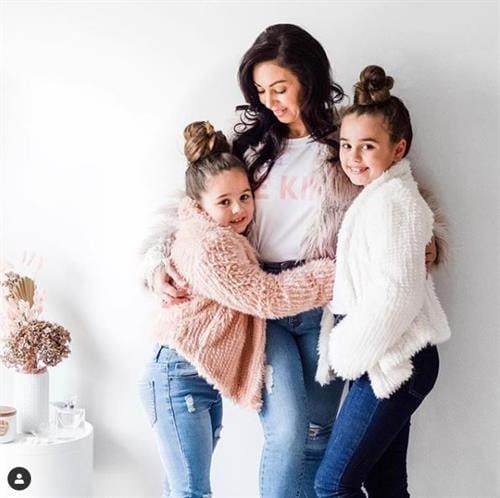 Aussie influencer Sandi wearing denim and a fluffy jacket while hugging her daughters Bella and Gigi