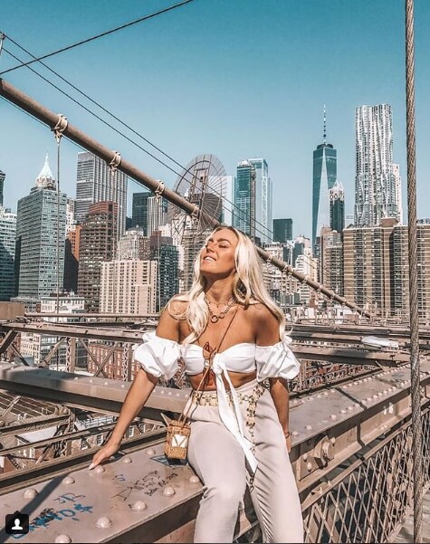 Influencer Angelica Blick sitting on bridge in cream top and pants