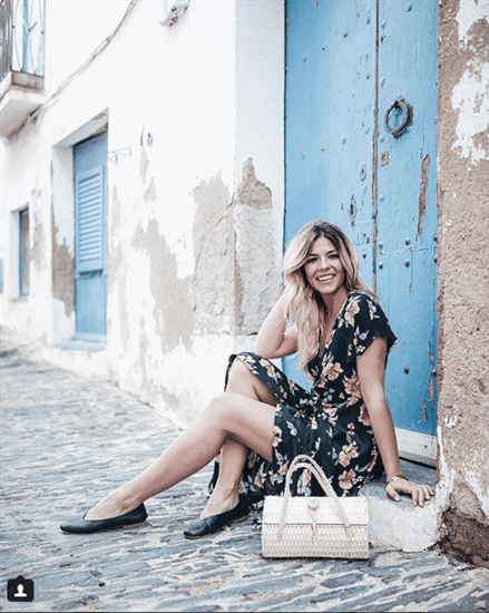 Influencer Natalia Cabezas sitting on door ledge in floral dress with black leather flats