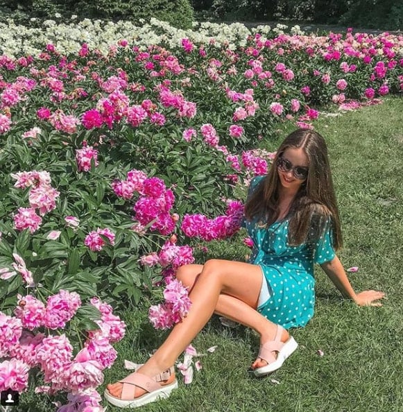 Influencer Gabriela Grebska laying in grass in front of pink flower garden