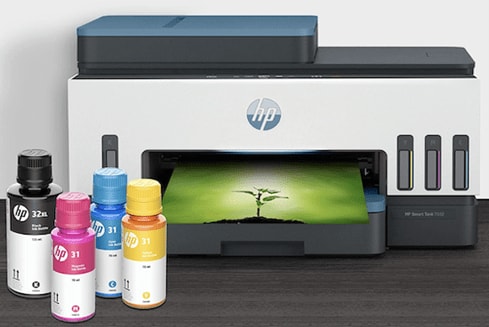 A white and black HP Smart Tank 7602 Wireless All-in-One Cartridge-Free Ink Tank Printer with a picture of a green tree and four cartridges of yellow, blue, pink, and black ink on a grey wooden panel