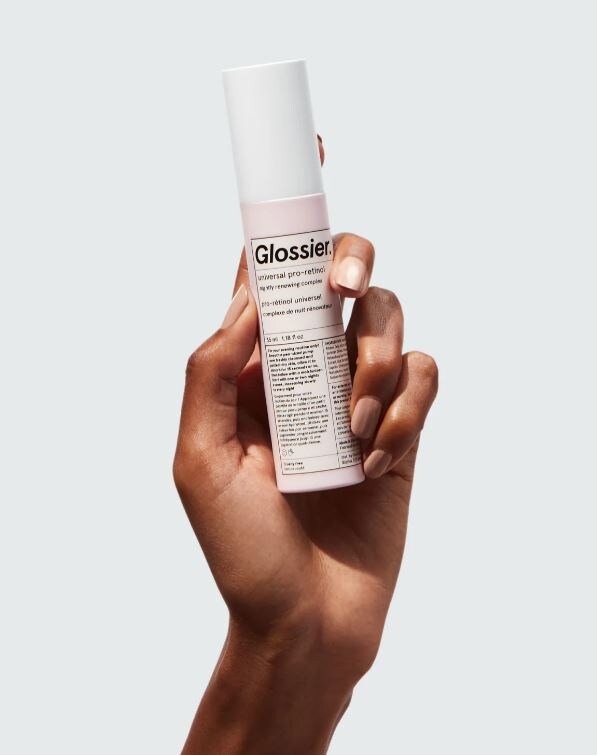woman holding a pink and white container of glossier retinol