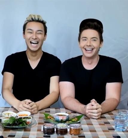 South Korean influencers Xander and Haeppy sitting next to each other in front of a table of food and laughing
