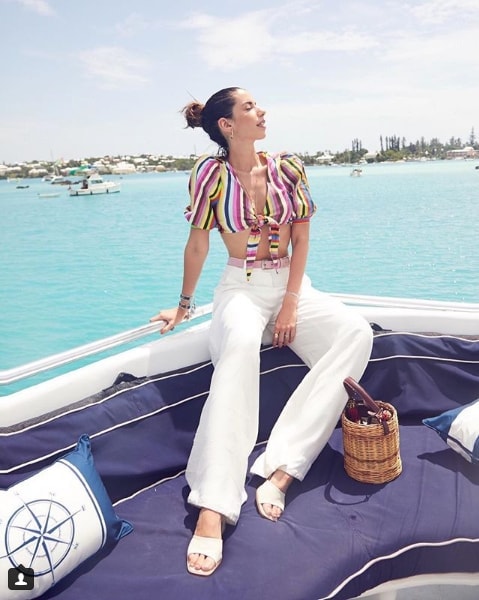 Influencer Camila Coutinho sitting on boat wearing striped crop top and white pants