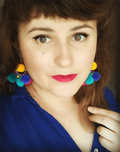 Influencer Gabriela Francuz taking selfie in blue top and colorful earrings with fuzzy balls