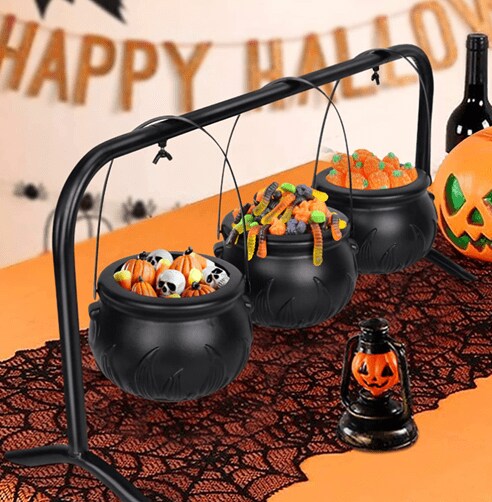 Three cauldrons filled with Halloween candy and placed on an orange table with a spiderweb-like tablecloth