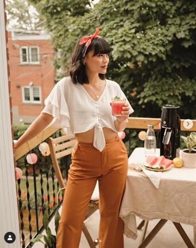 Canadian influencer Katie Cung enjoying a drink on her balcony in a cropped blouse and wide leg trousers