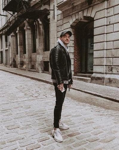 Canadian influencer Dan Gabrielli posing on a cobblestone street in jeans, hoodie, leather jacket, and baseball cap