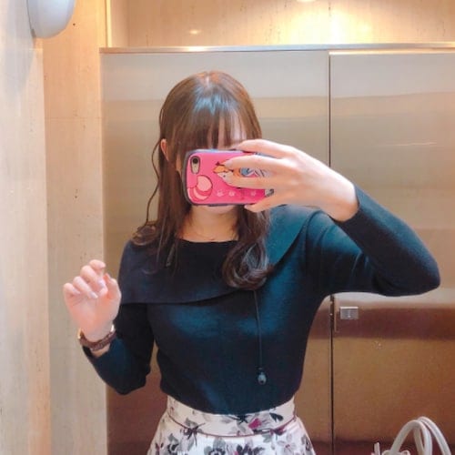 Rio Hitorigurashi wearing a navy long-sleeve top and white pants and holding a pink phone in front of her face