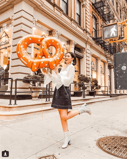 Influencer Olivia Lazuardy holding giant pretzel balloon wearing black skirt and white boots