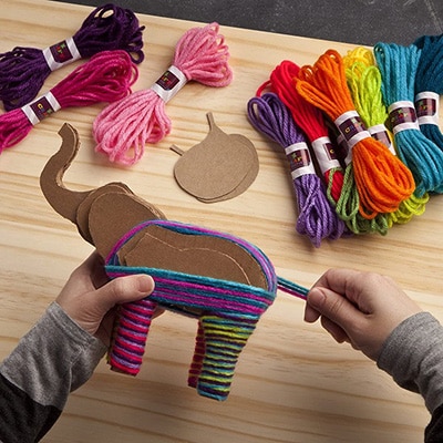 Child's hands wrapping yarn around a cardboard elephant