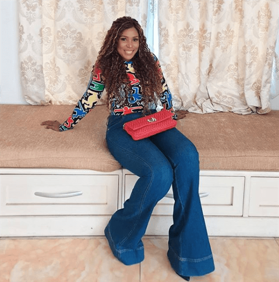 Nigerian blogger Linda Ikeji in jeans and printed top sitting in a window seat