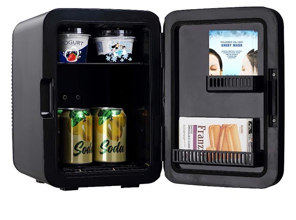An open, black Amazon mini fridge. Inside there are a couple of beers and yoghurts, as well as a chocolate bar and a sheet mask in the mini compartments. 