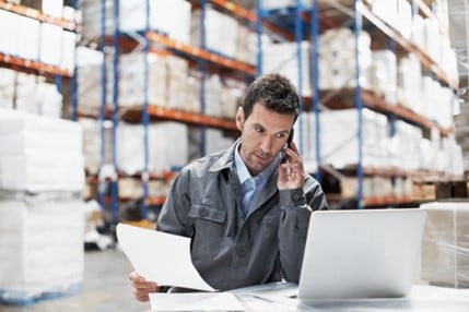 Businessman holding paperwork and talking on the phone in a shipping warehouse