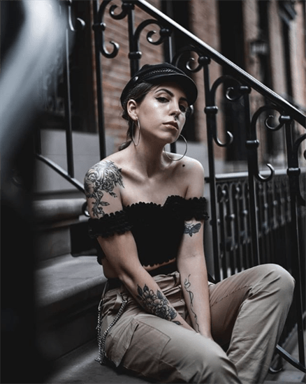 Blogger Lessie wearing black off the shoulder top sitting on staircase with tattoos on body