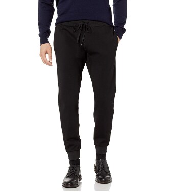 a man donning a pair of black Theory Vault Jogger pants with a drawstring, navy blue sweater hoodie, black socks, and black dress shoes
