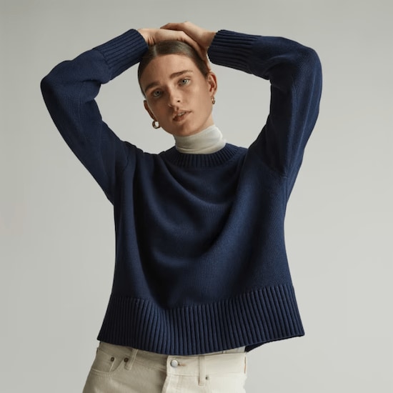 A woman wearing a Navy Everlane Organic Cotton Crew Sweater with a white turtleneck shirt and beige pants