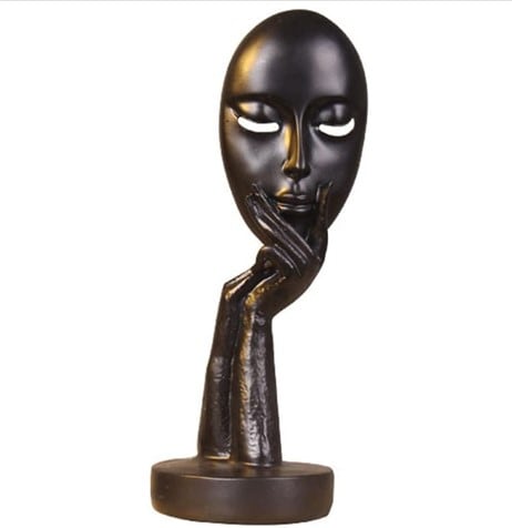 A black resin statue of a hand holding a female face mask with closed eyes