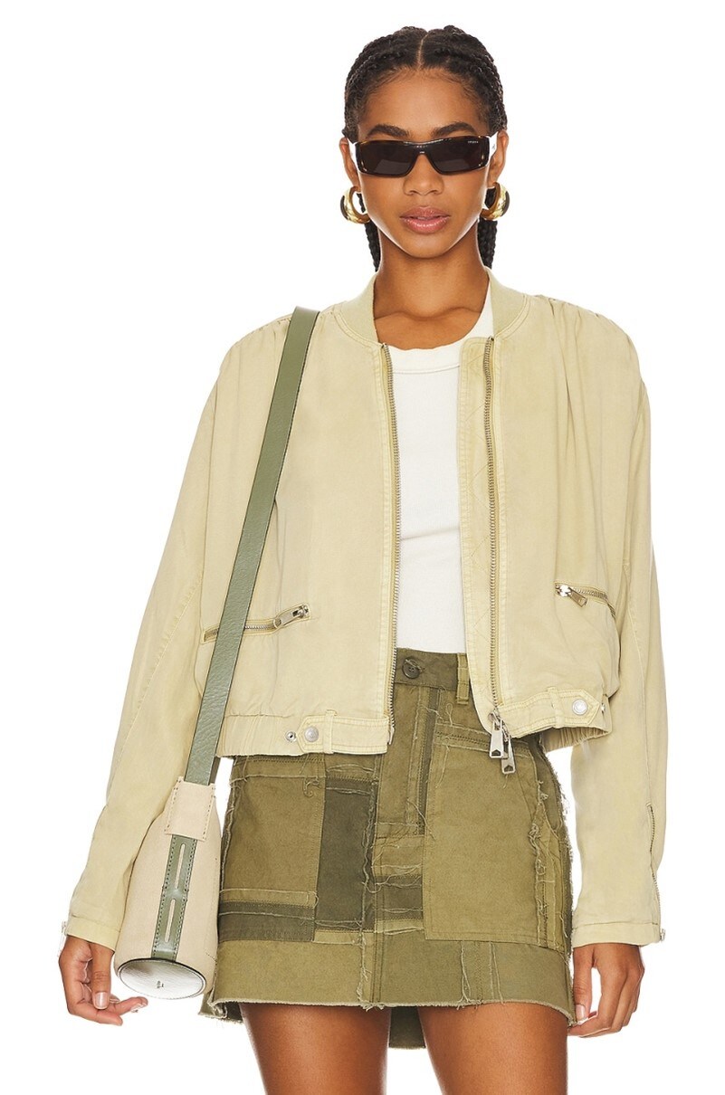 Model wearing the neutral Revolve siren bomber jacket paired with a white t-shirt, a dark green, patchy skirt and a beige bag