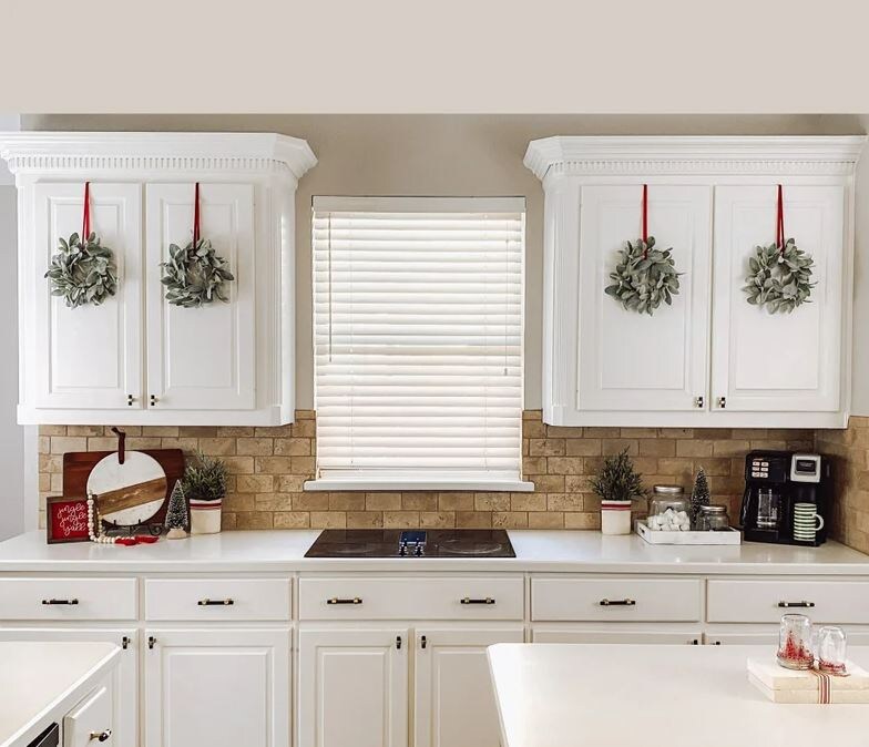 four mini wreaths with red ribbon hung from white kitchen counters