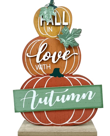 Three pumpkins of different sizes and colors stacked on top of each other with the words “Fall in love with autumn” written on them