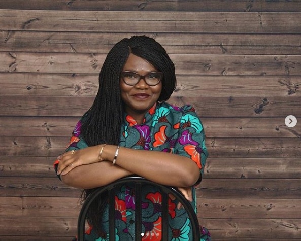 Nigerian food blogger Nma sitting in front of a rustic wood wall in a bright floral print shirt 