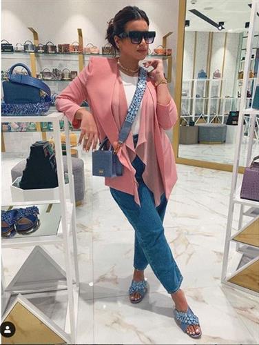 Fashion and beauty influencer Amal Al Aradi posing in a boutique in denim, sandals, and a pink cardigan