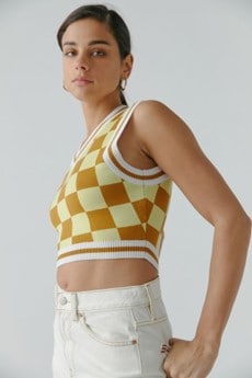 Model wearing checkered UO Randi Shrunken Sweater Vest in the color Gold, combined with white jeans