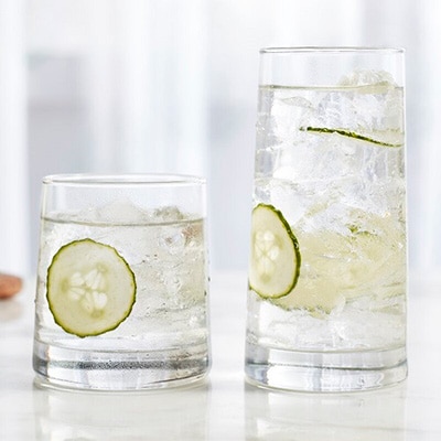 One tumbler and one rocks glass of Libbey Cabos’s set filled with transparent liquid ice cubes and cucumber slices.