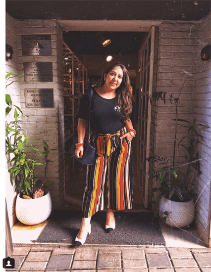 Blogger Nitika Bhatia posing in doorway wearing orange, brown, and yellow striped pants