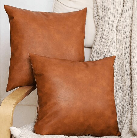 Two pillows in brown leather throw pillowcases on a white chair