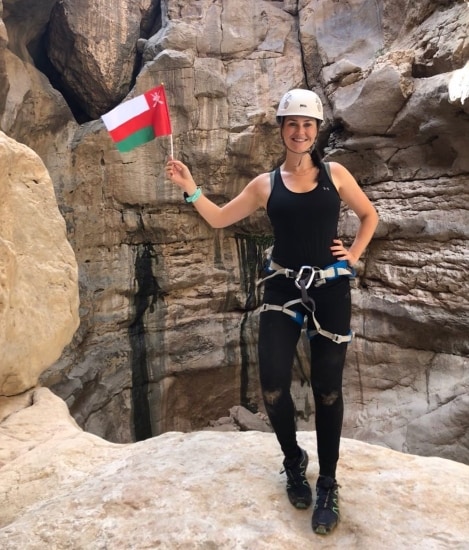 Heather Duncan, an Omani blogger, holding up the Oman flag while rock climbing