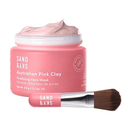 A small pink application brush in front of an open pink container of Sand & Sky’s Australian Pink Clay mask