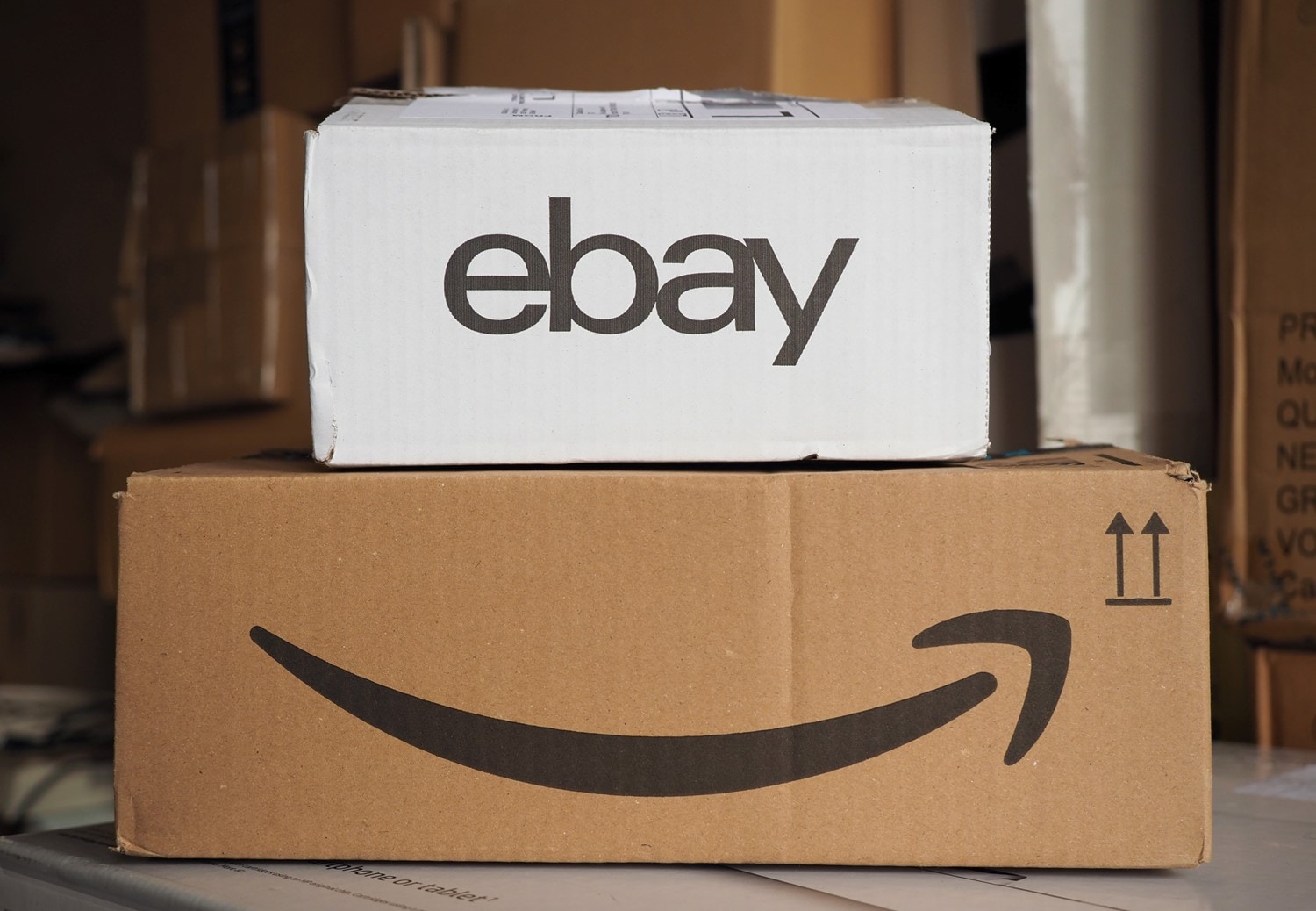 A smaller boxed package with the eBay logo sitting on top of a larger boxed package with the Amazon arrow graphic.