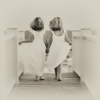 two girls in white sundresses walking down an wooden pathway to a beach 