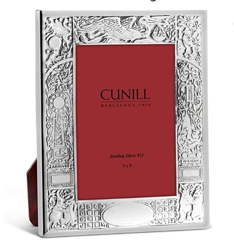A beautifully engraved silver photo frame with a red paper inside and the picture size and name of the brand, Cunill, printed on it in black.