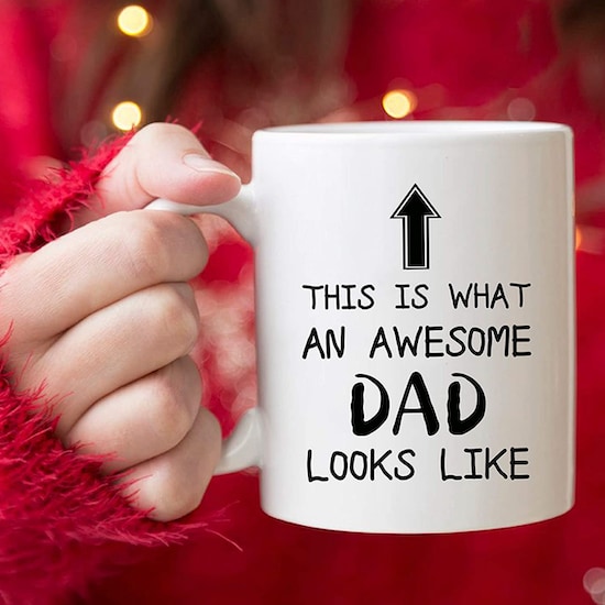 A white 5Aup Funny Dad Mug with black words print being held by someone wearing a red furry outfit