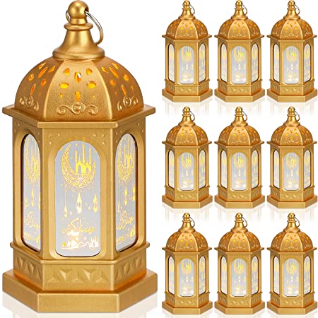 Two gold Dandelionwall LED Decorative Ramadan Candles and Lanterns on top of gold and white platforms next to shiny white and gold presents