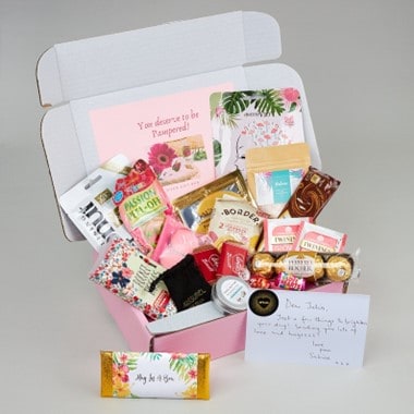 A pink box with sweets, self-care items, and a personalized card