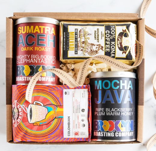A cardboard box with Indonesian Sumatra Aceh, Ethiopian Yirgecheffe, Organic Fair Trade Colombia and Kona Coffee bags and cans for coffee lovers